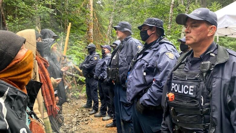 A row of protesters stands face-to-face with a row of police officers in a forest. 