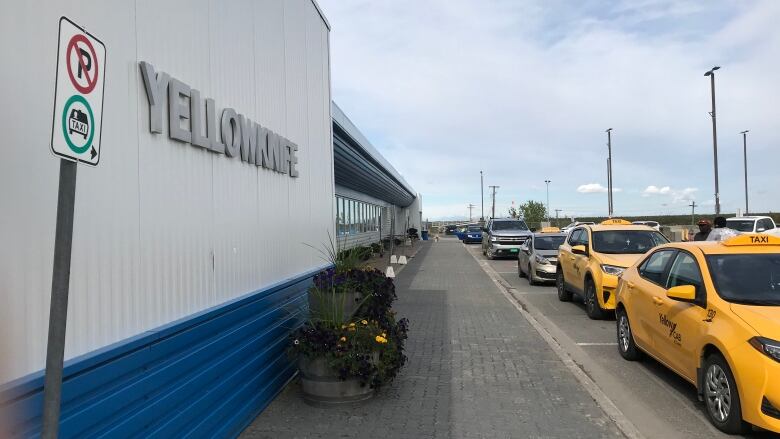 Yellow cars line up in front of a building on a sunny day. 