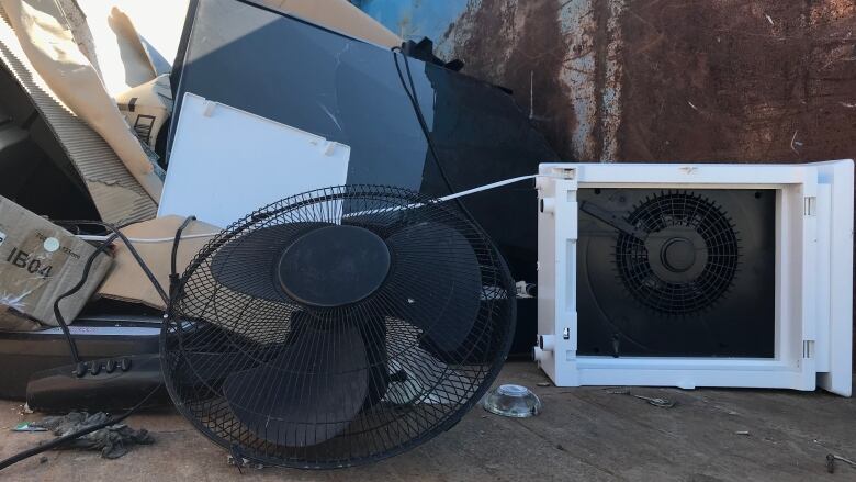 A TV and a fan, among other electric items, in a dumpster.