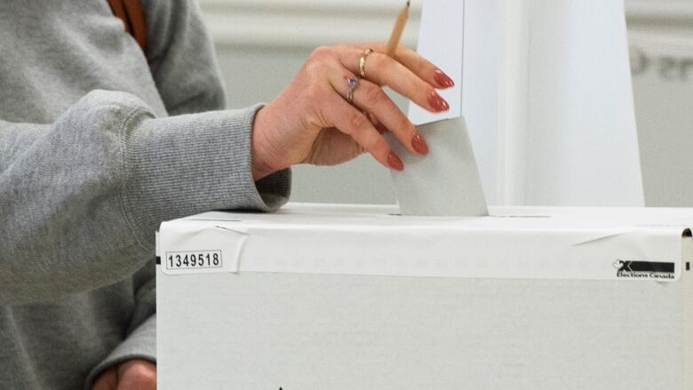 A person puts a ballot into the top of a ballot box.