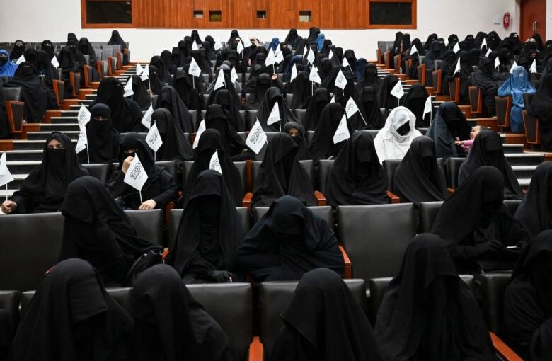 A group of people in black veils sit in a lecture hall.