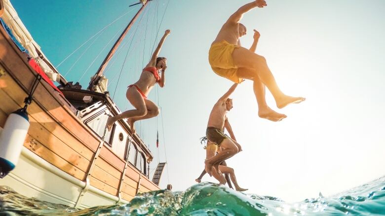 People in swimsuits jump off a yacht into water on a sunny day.