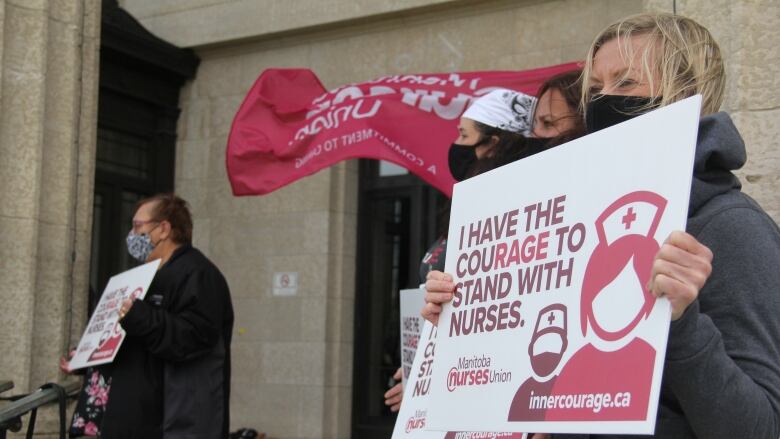 A woman in a grey sweater holds a white signs that reads, 