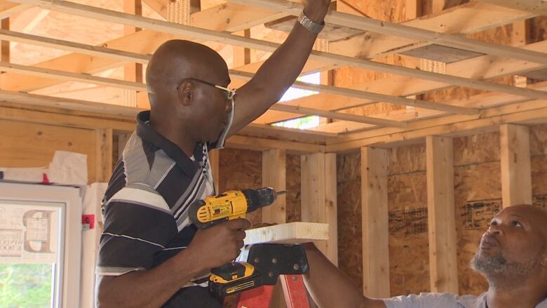 A Black man holding a drill working working on a house frame