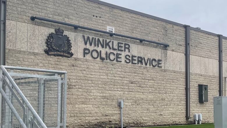 The exterior of a grey brick building shows a 'Winkler Police Service' sign.