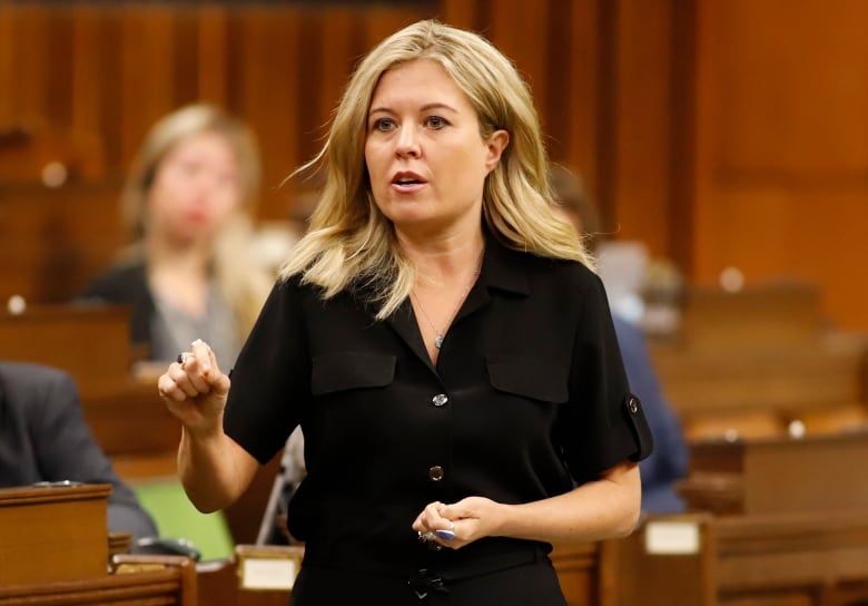 A woman in a black dress gestures while speaking.