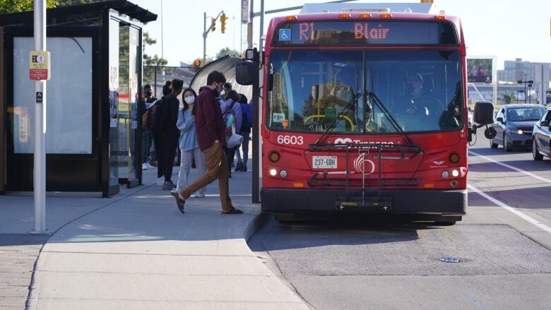 People wearing face masks walk onto a red bus