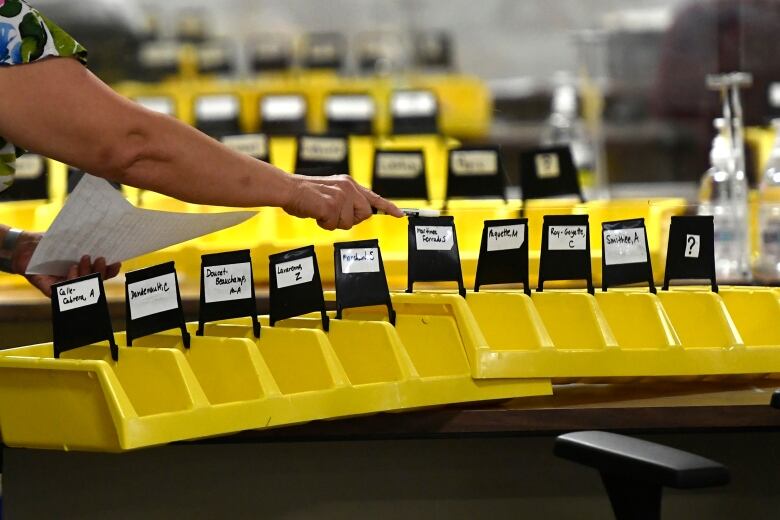 A worker organizes bins labelled with the names of candidates into which special ballots from national, international, Canadian Forces and incarcerated electors will be placed and counted, at Elections Canada's distribution centre in Ottawa on election night of the 44th Canadian general election, on Monday, Sept. 20, 2021.