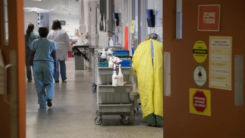 Open doors showing a hospital hallway, with four health-care workers from behind.