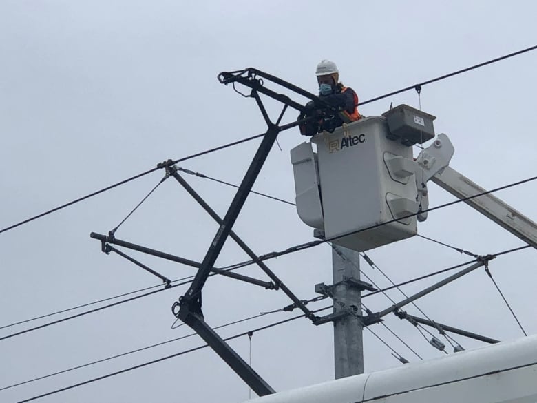 A worker in a bucket truck works on a power system above a public transit train.