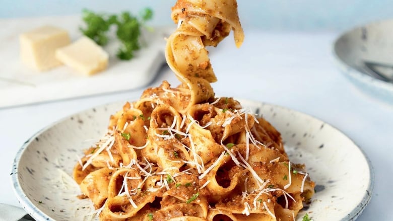 Closeup on a plate of pasta with bolognese sauce on it. A noodle is twirled on a fork above the plate. 