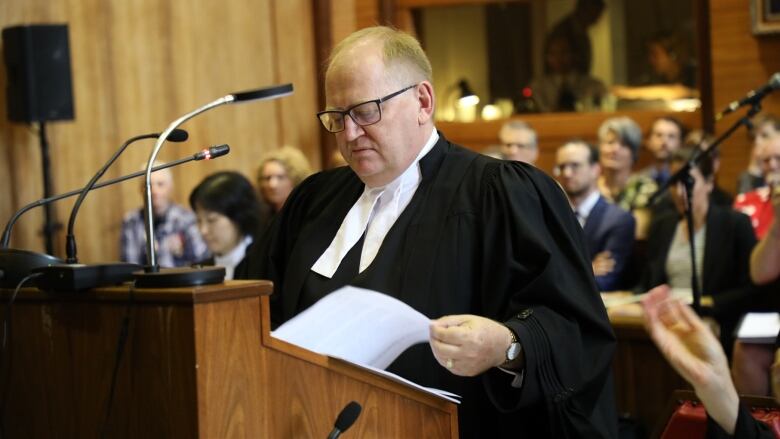 A lawyer wearing a black robe, standing behind a podium. 