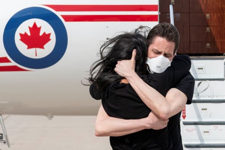 A man and woman hug tightly at the bottom of an airplane's ramp.