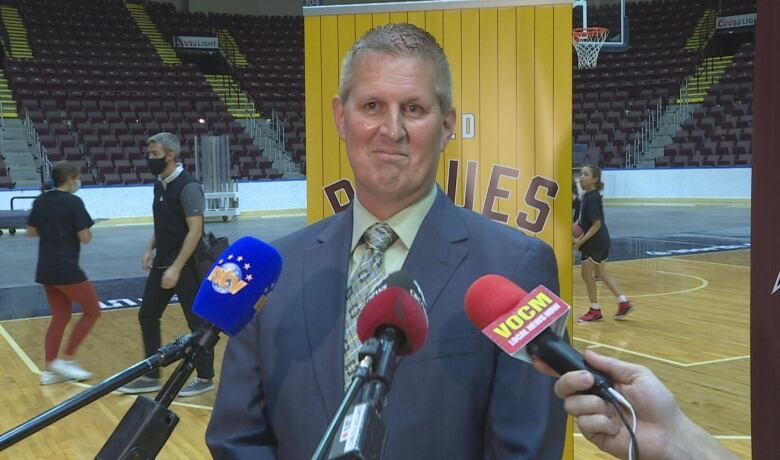 Man with several microphones in front of him. He is wearing a blue suit. 