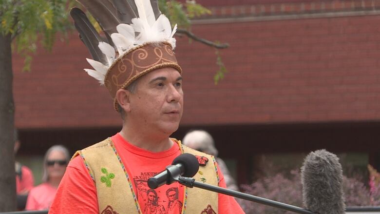 Man speaking at a podium, wearing headdress