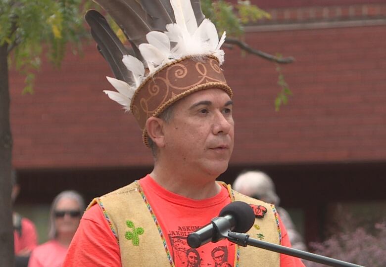 Man speaking at a podium, wearing headdress