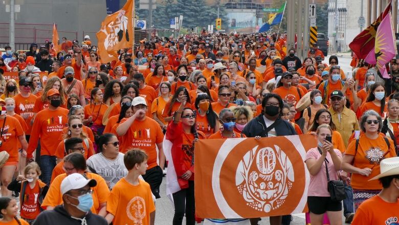 People wearing orange shirts and orange flags walk down a street in Manitoba for National Day for Truth and Reconciliation day.