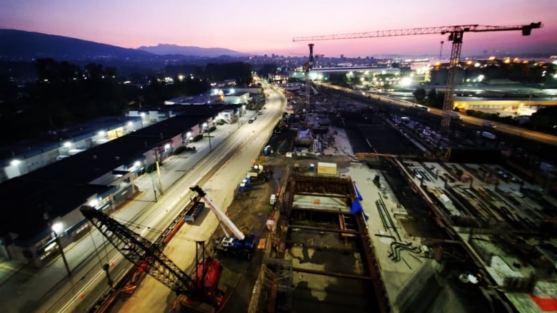 A construction site with a crane, heavy equipment and a sunset in the background, shows the very early stages of the plant's construction.