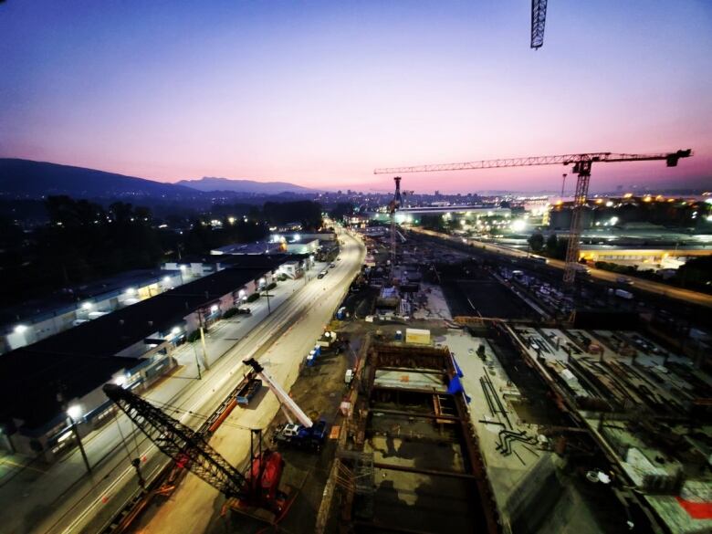 A construction site with a crane, heavy equipment and a sunset in the background, shows the very early stages of the plant's construction.