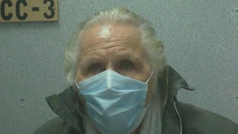 A white-haired man wears a surgical mask in a screen shot from a video call.