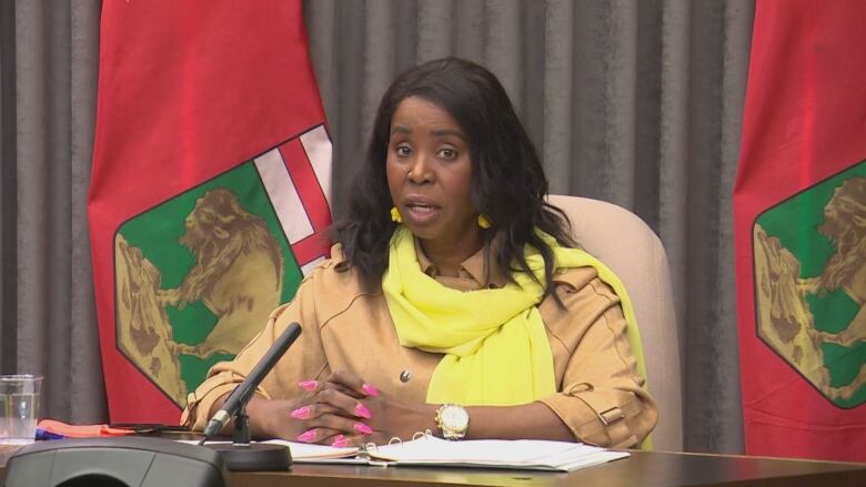 A woman speaks as a news conference while sitting behind a desk with a microphone. 