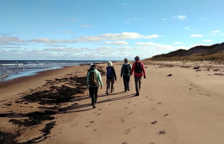 People dressed for a long hike walking along a sandy beach. 