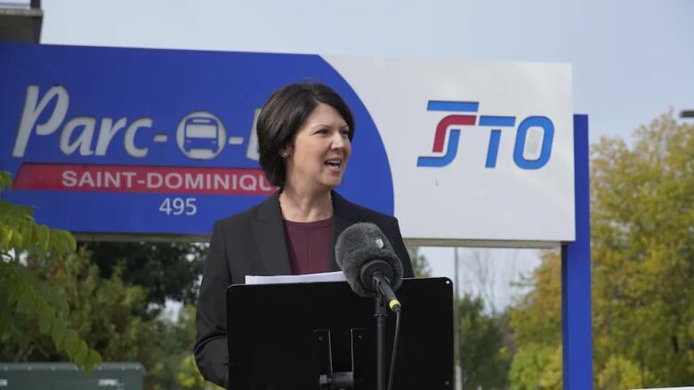 A woman stands at a podium, speaking into a microphone 