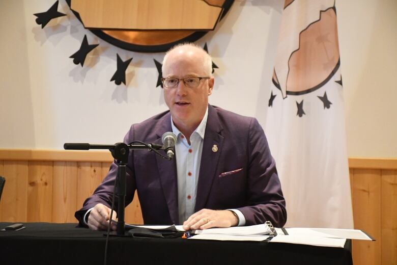 A man sits at a table speaking into a microphone.