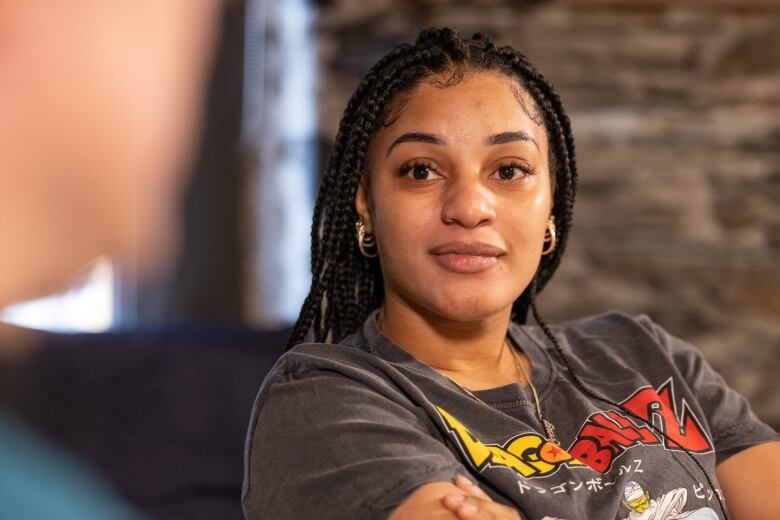 A woman wearing a Dragon Ball Z shirt with crossed arms smiles while looking at the camera. 