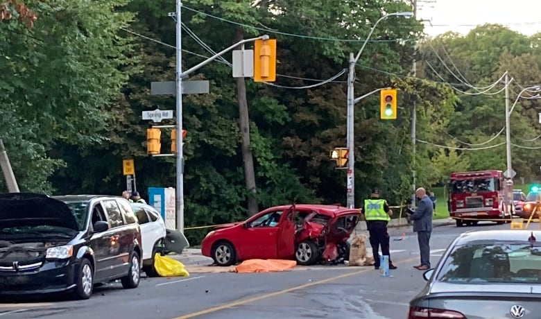 Police stand by a smashed up red car on a major road. Other damaged vehicles are stopped on the road.