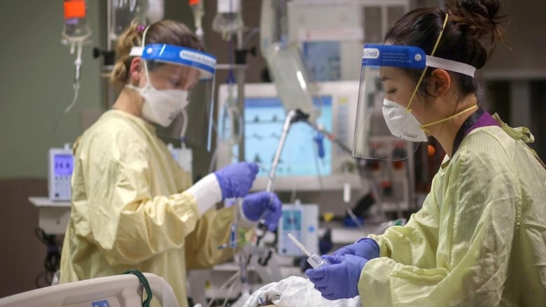 Health care workers in masks and face shields care for a patient in the ICU