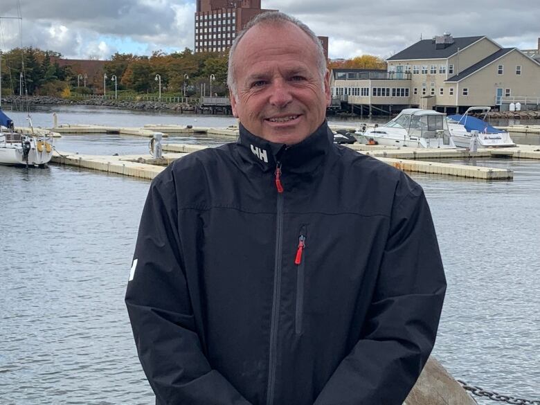 A man with short cropped hair and a dark blue Helly Hansen jacket with a view of Charlottetown Harbour in the background.