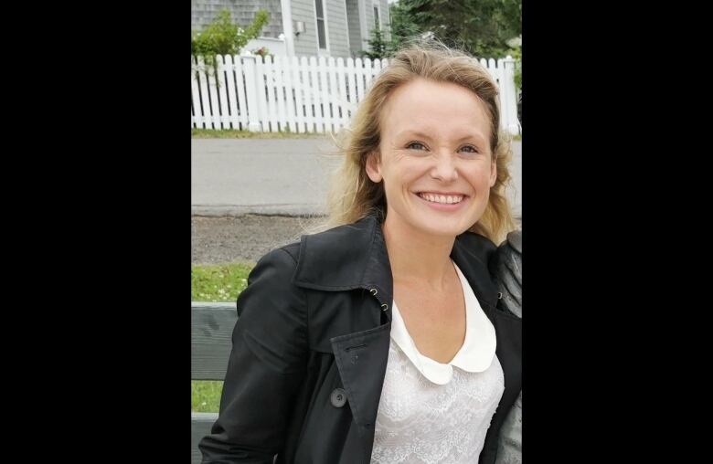 A woman with blonde hair, a black jacket and white lace blouse smiles.