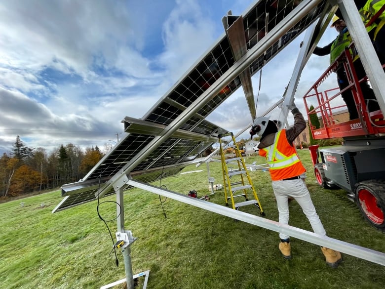 Man in safety vest stands under a huge inclined solar panel