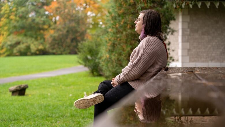 A woman with long brown hair and glasses sits at picnic table at a park. 