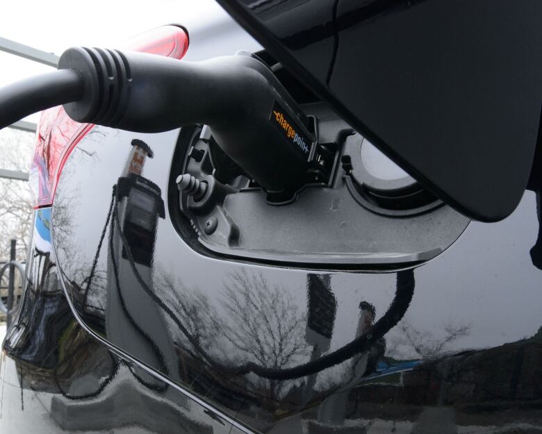 A charging handle is inserted into the port of a white electric car.