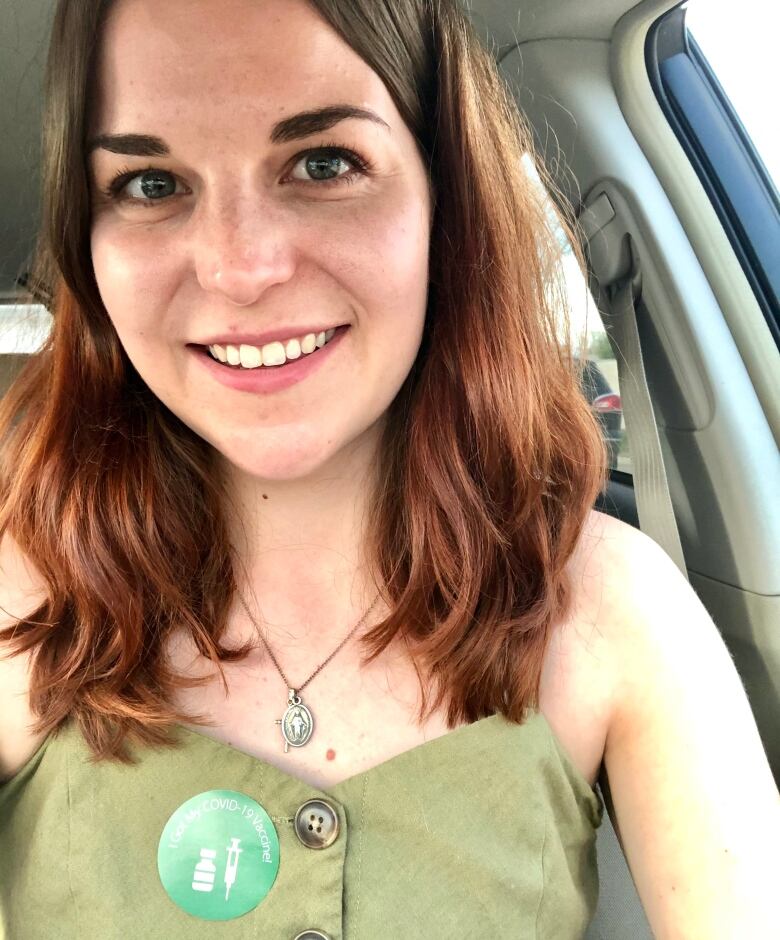 Woman with long dark hair smiles at camera while sitting in a car