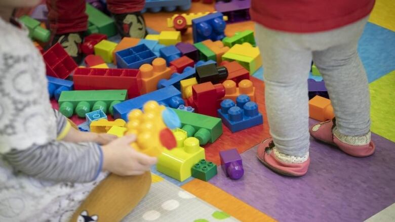 Two unidentifiable children stand amongst Duplo blocks.  