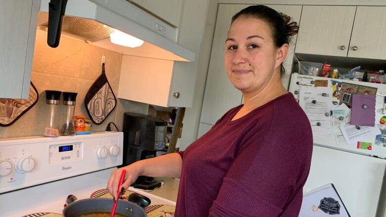 A woman stands at a stove, stirring a pot of soup.