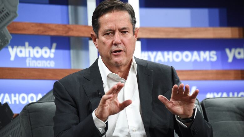 A man a dark suit and white shirt speaks at a financial summit.