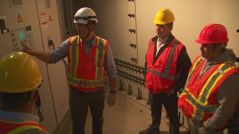 Four men in construction hats and vests gather at computer panel.