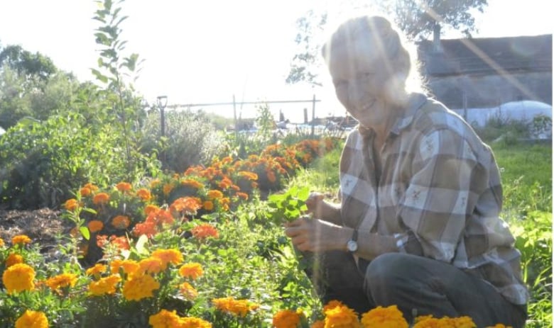 A farmer poses next to a garden.