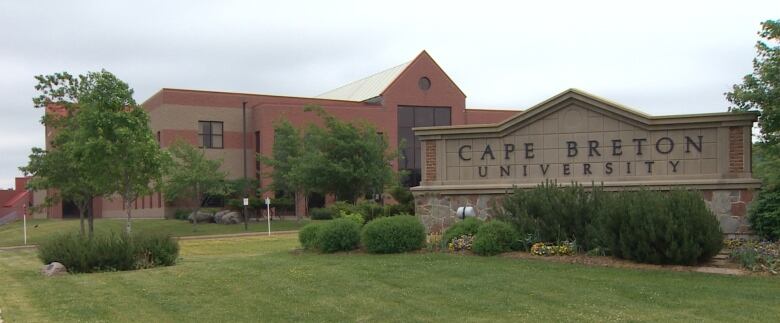 A red brick sign says Cape Breton University in front of a red brick building.