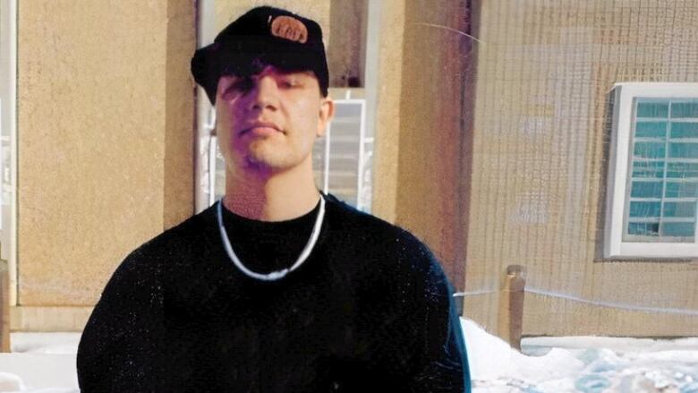 A man stands in front of a prison with his hands folded in front of him. 