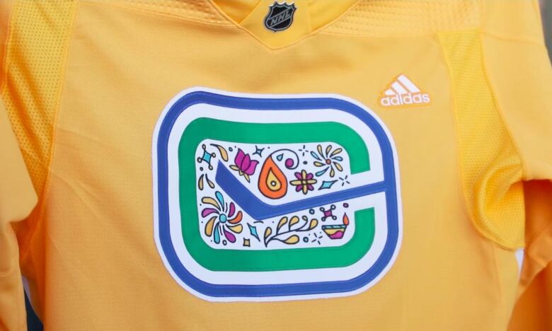 A close up photo of a bright yellow Vancouver Canucks jersey with a colourful Diwali-inspired design.