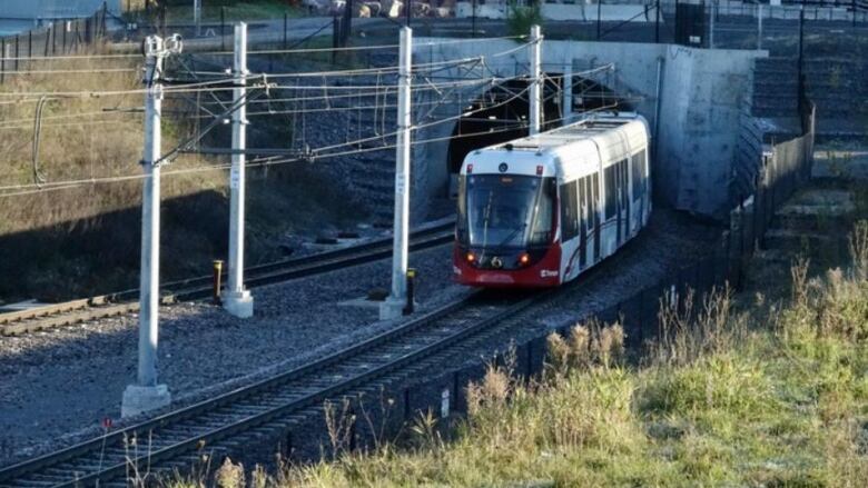 A red and white light rail train emerges from a tunnel.