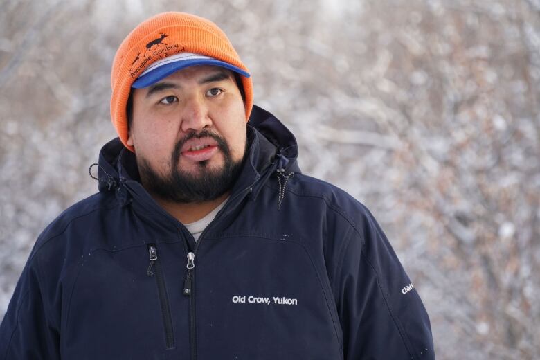 A man with a winter coat and hat is visible in the winter woods.