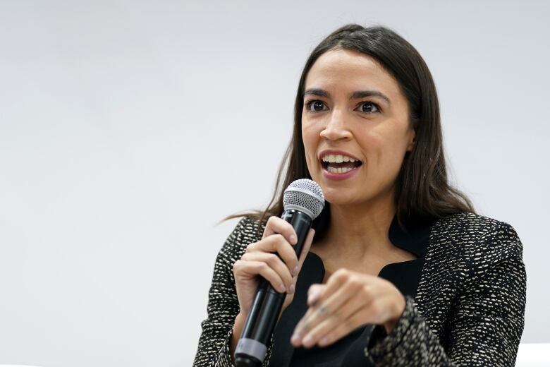 Woman with long dark hair and wearing grey suit jacket speaks into a microphone.