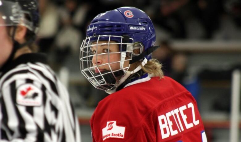 A female hockey player wearing a red jersey looks off in the distance.