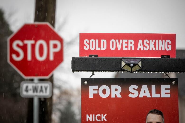 A real estate sign that reads 'SOLD OVER ASKING' just atop a sign that reads 'FOR SALE'.